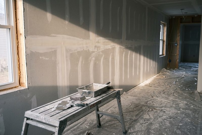 Pared interior con paneles de drywall instalados y segunda capa de compuesto aplicada sobre las juntas