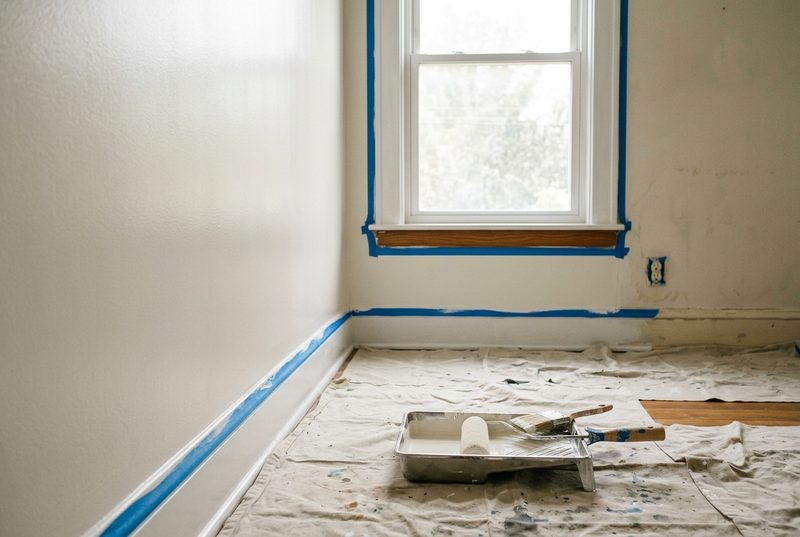 Habitación en proceso de pintura con cinta azul de enmascarar en zócalos y marco de ventana